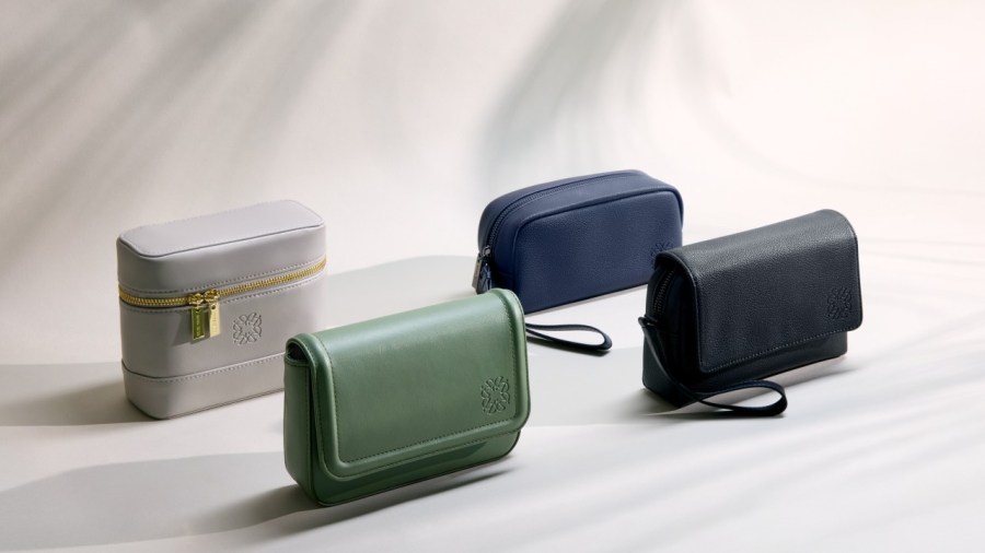 An arrangement of four distinct amenity kits featuring various designs in colors including white, green, navy, and black. Each kit showcases a stylish and elegant look, with some featuring a detachable strap and a textured finish.