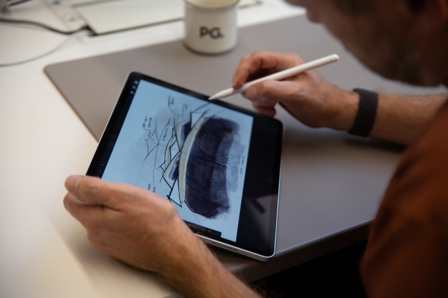 A person using a tablet with a stylus to create digital sketches in a design studio setting.