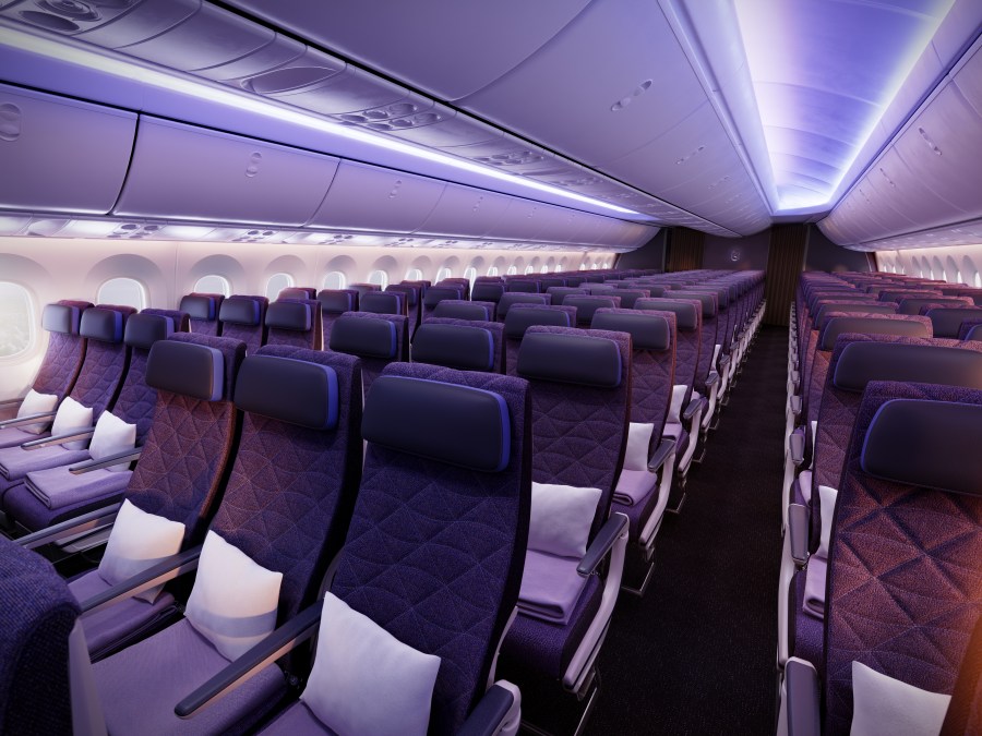 Interior view of a modern airplane cabin featuring rows of purple upholstered seats, accented with white pillows and ambient lighting.